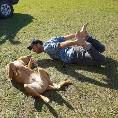 Candid photo of Jason Rahilly from B-Alternative, rolling on the grass with his dog.
