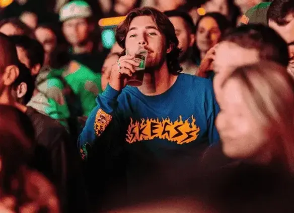 A man drinks from a reusable cup in a crowd at a large music event, with the cup showing custom printing.