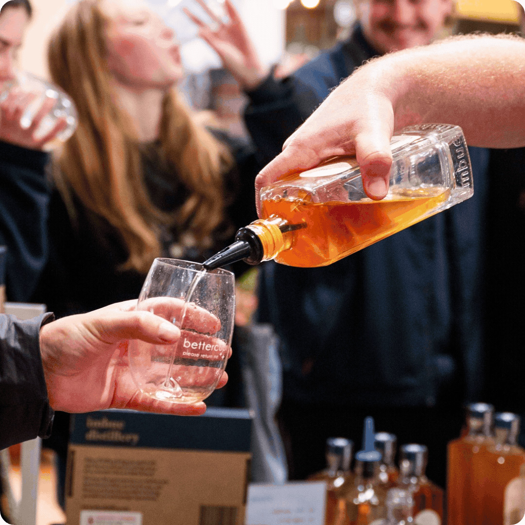 Person pouring whiskey into a glass at a social gathering, with people in the background.