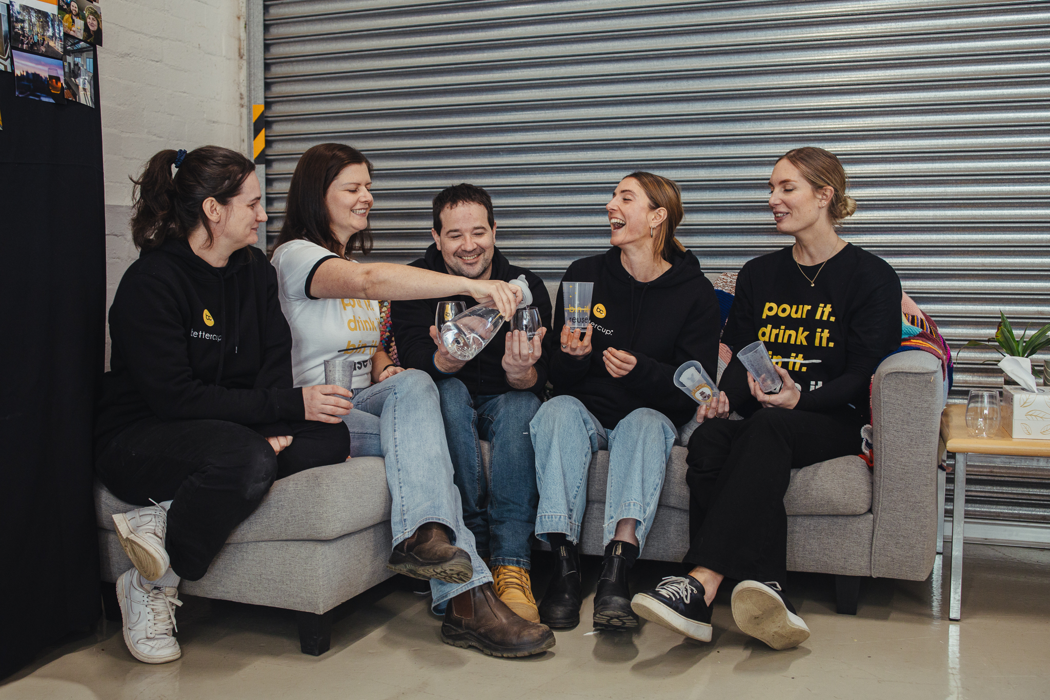 Bettercup team seated together on a couch as Rachel pours drinks into their bettercup tumblers.